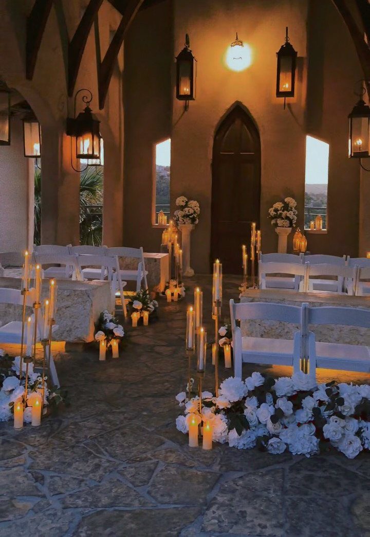 Open-air chapel with white chairs, glowing candles, and white flowers on stone floors.