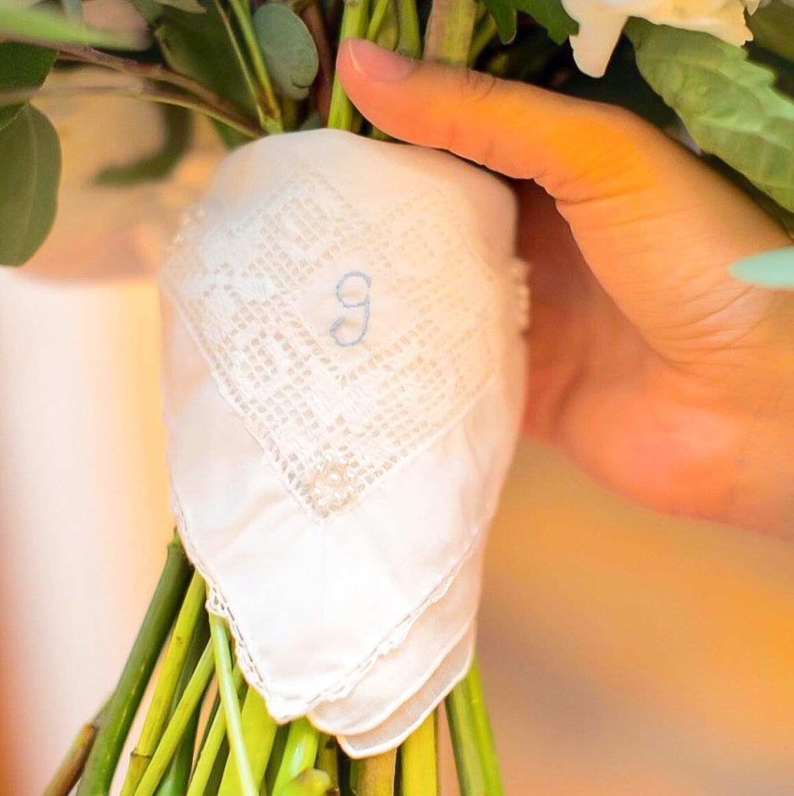 White lace bouquet wrap with a small blue embroidered letter g on it.
