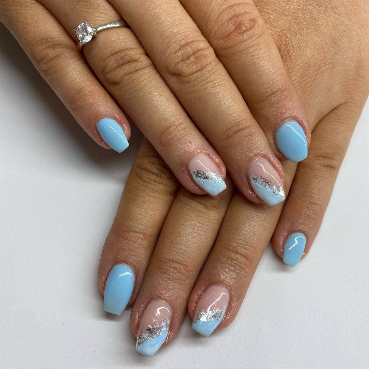 Light blue manicured nails with silver glitter accents and a diamond engagement ring.