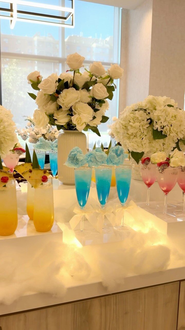 Blue signature cocktails in champagne flutes on a white bar with white flowers.