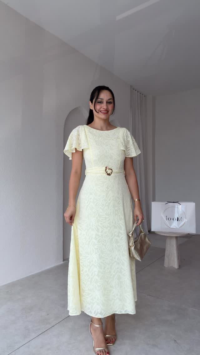 Woman in a pale yellow midi dress with flutter sleeves and gold accessories.