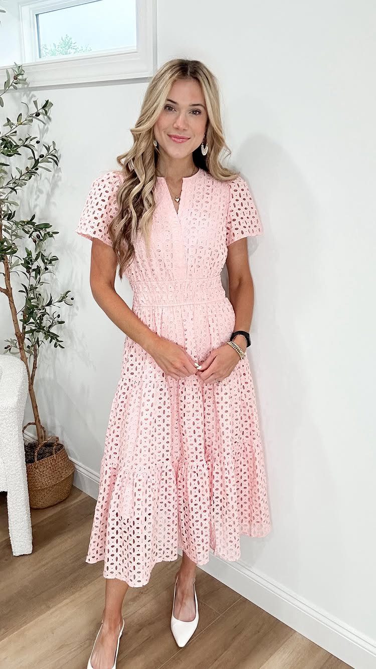 Woman wearing a light pink eyelet lace midi dress with short sleeves and white heels.