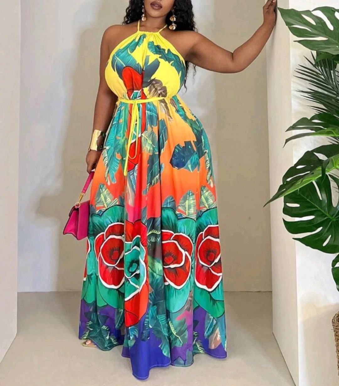 Woman in a colorful tropical floral maxi dress holding a pink handbag.