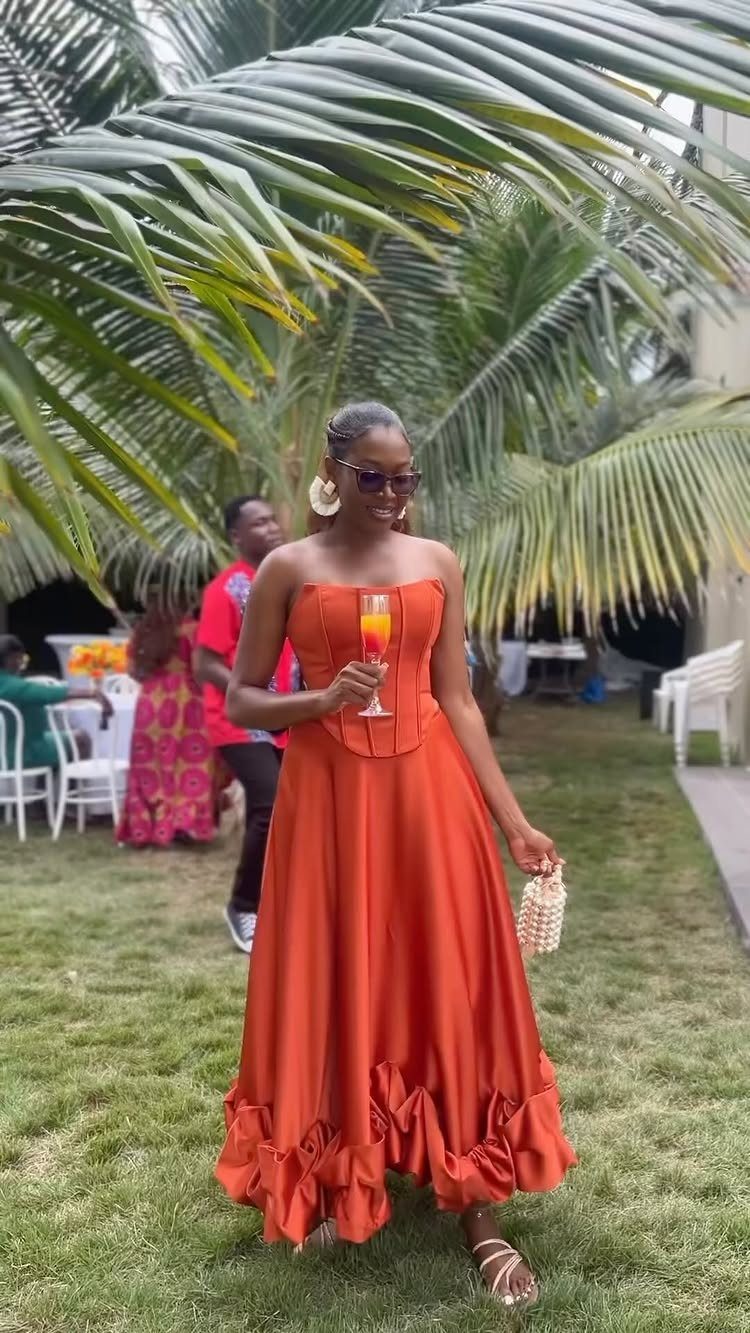 Woman in a strapless orange satin maxi dress standing under tropical palm trees.