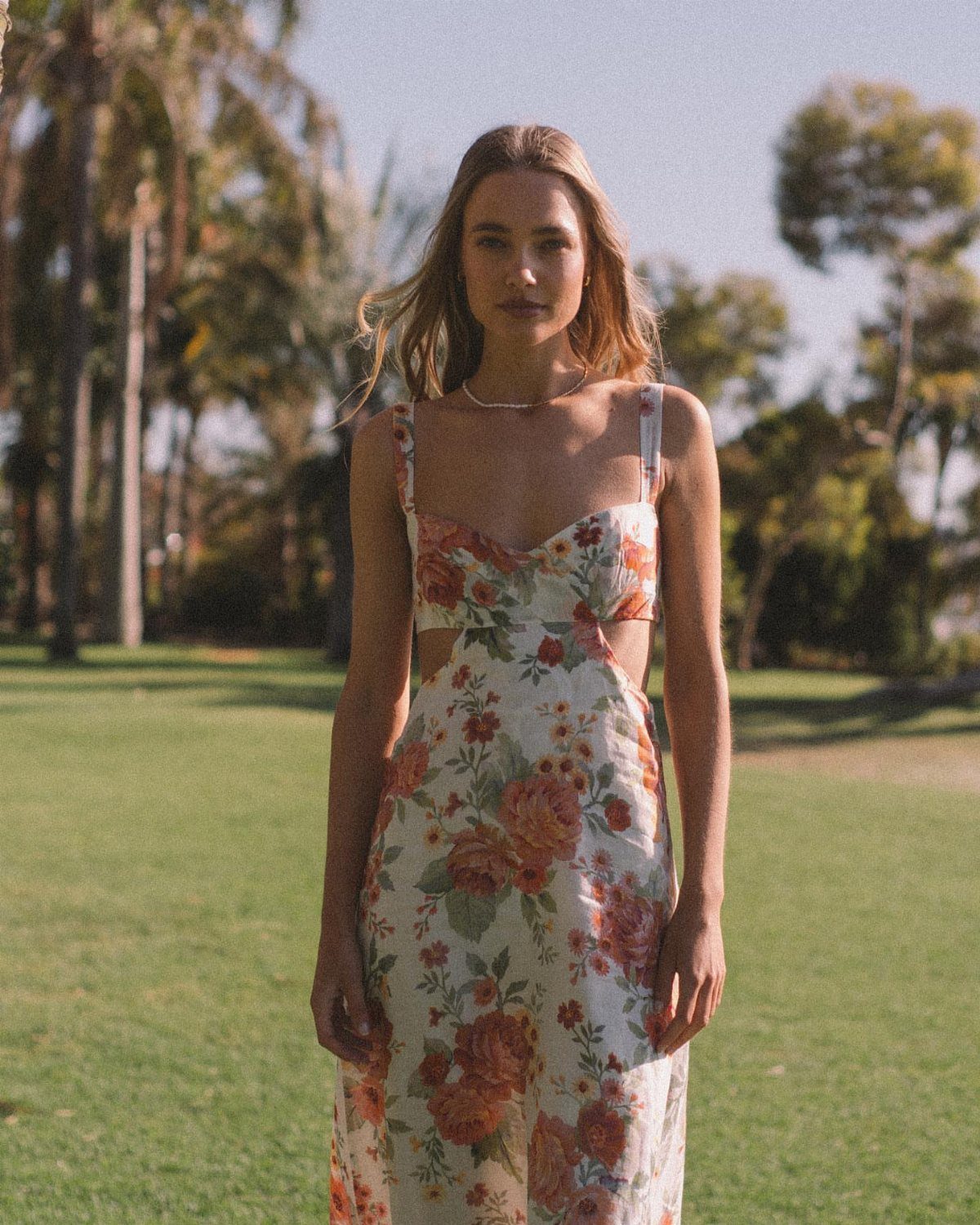 Woman in a white floral midi dress with cut-outs standing on a sunny lawn.