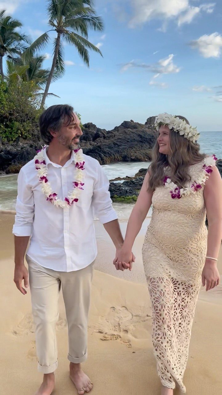 Barefoot couple in white beach attire holding hands on a tropical sandy shore