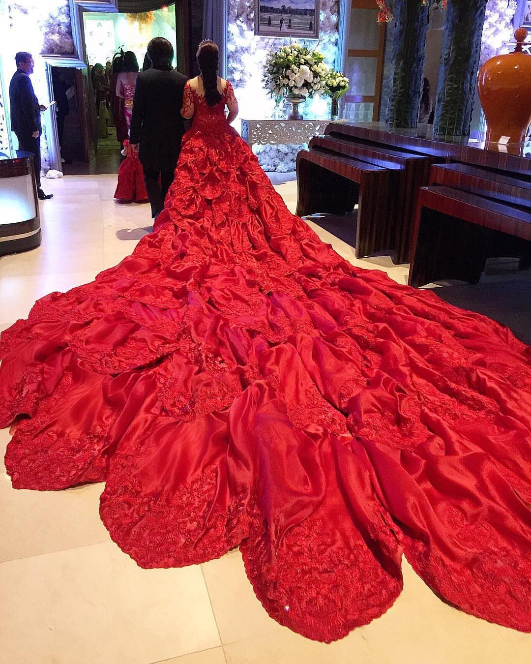 Woman wearing a voluminous bright red gown with a long lace embroidered train.