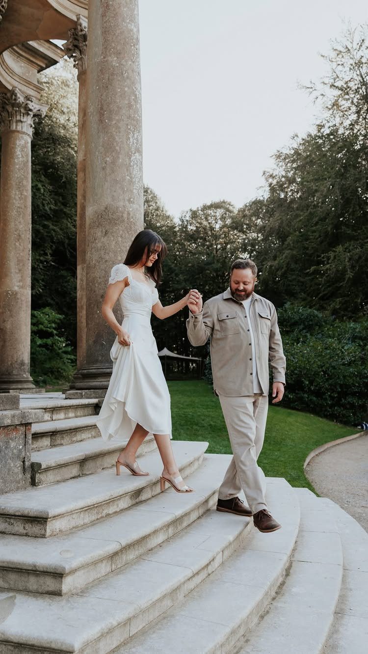 Couple holding hands walking down stone steps, woman wearing a casual white midi dress.