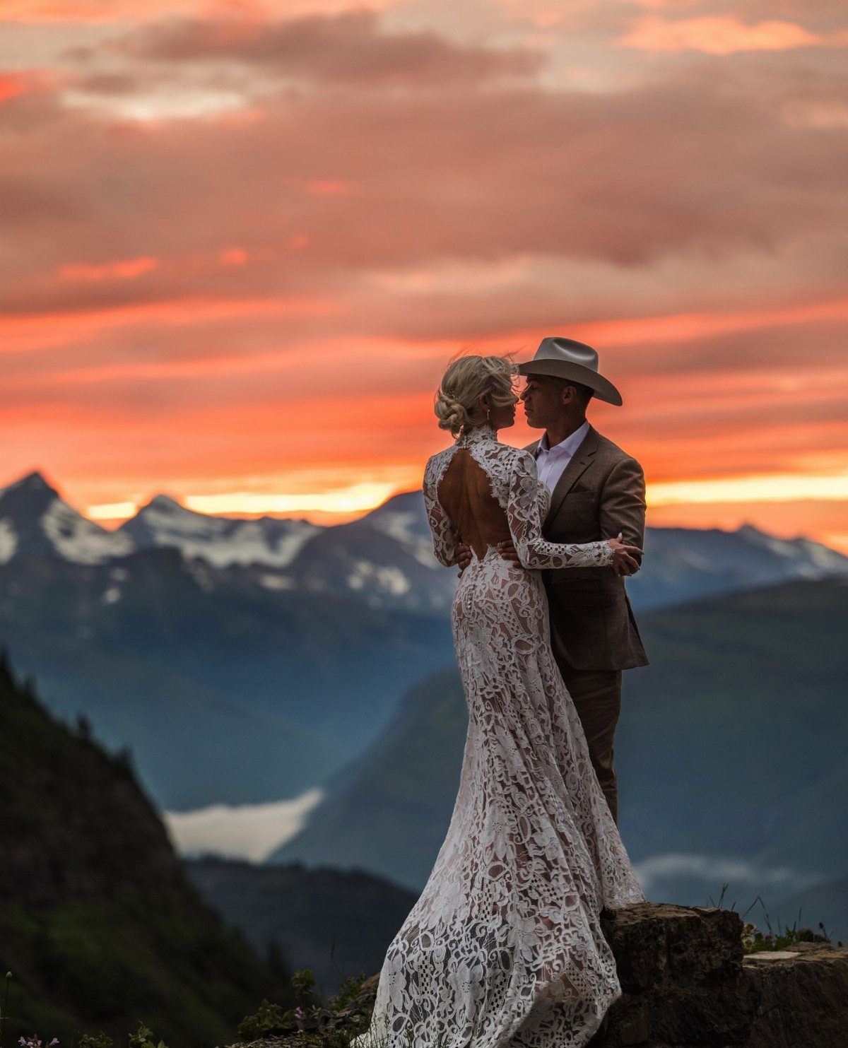Woman in ivory lace sheath dress embracing man in suit at mountain sunset