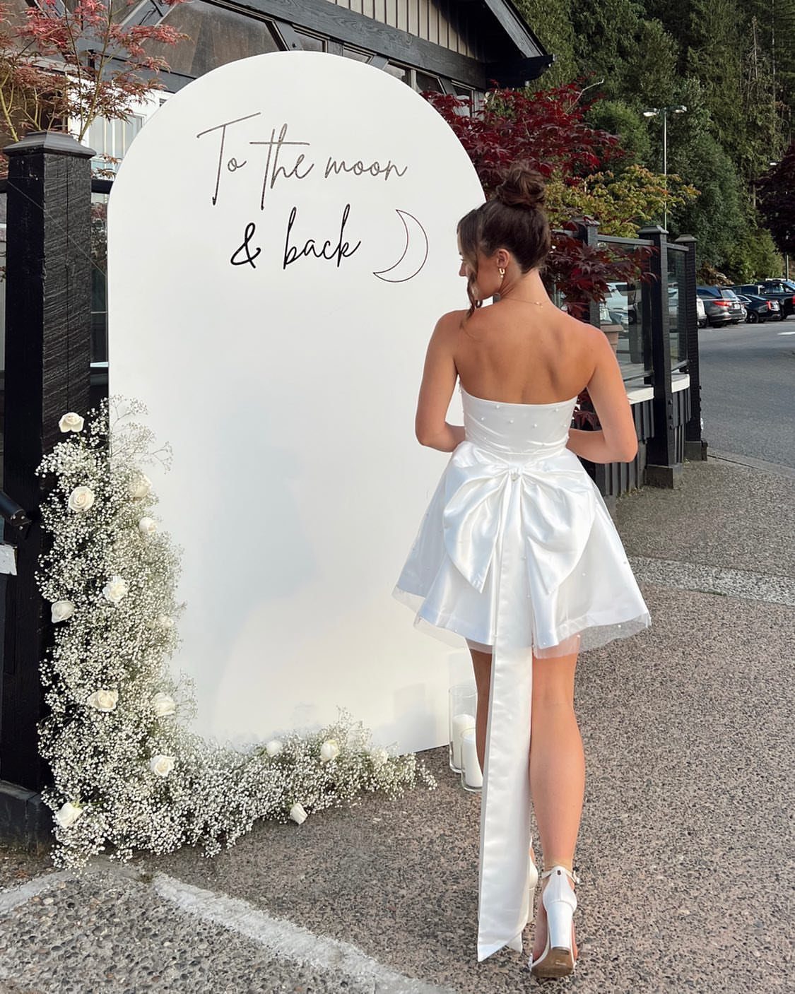 Woman in a short white strapless satin dress with a large back bow.