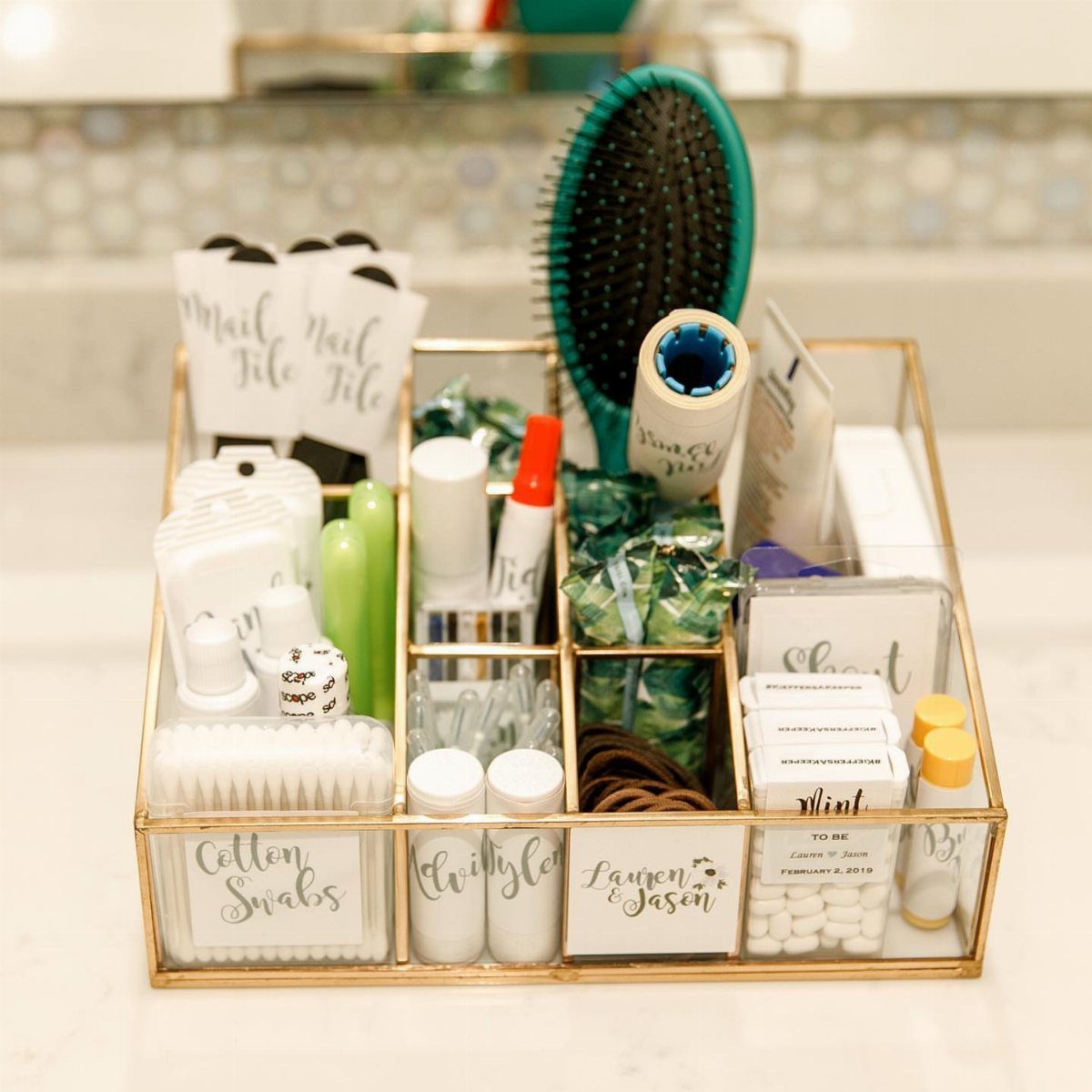 Gold bathroom basket filled with wedding guest toiletries and personalized labels on a counter