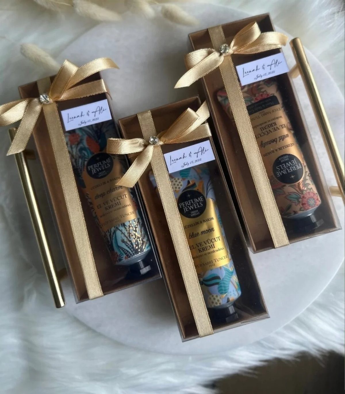 Three gold gift boxes with ribbons containing tubes of luxury hand cream.