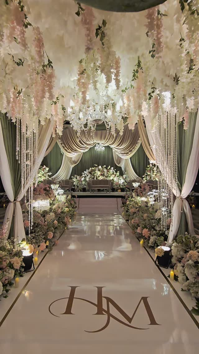 Wedding aisle with sage green curtains, hanging pink and white flowers, and gold monogram.