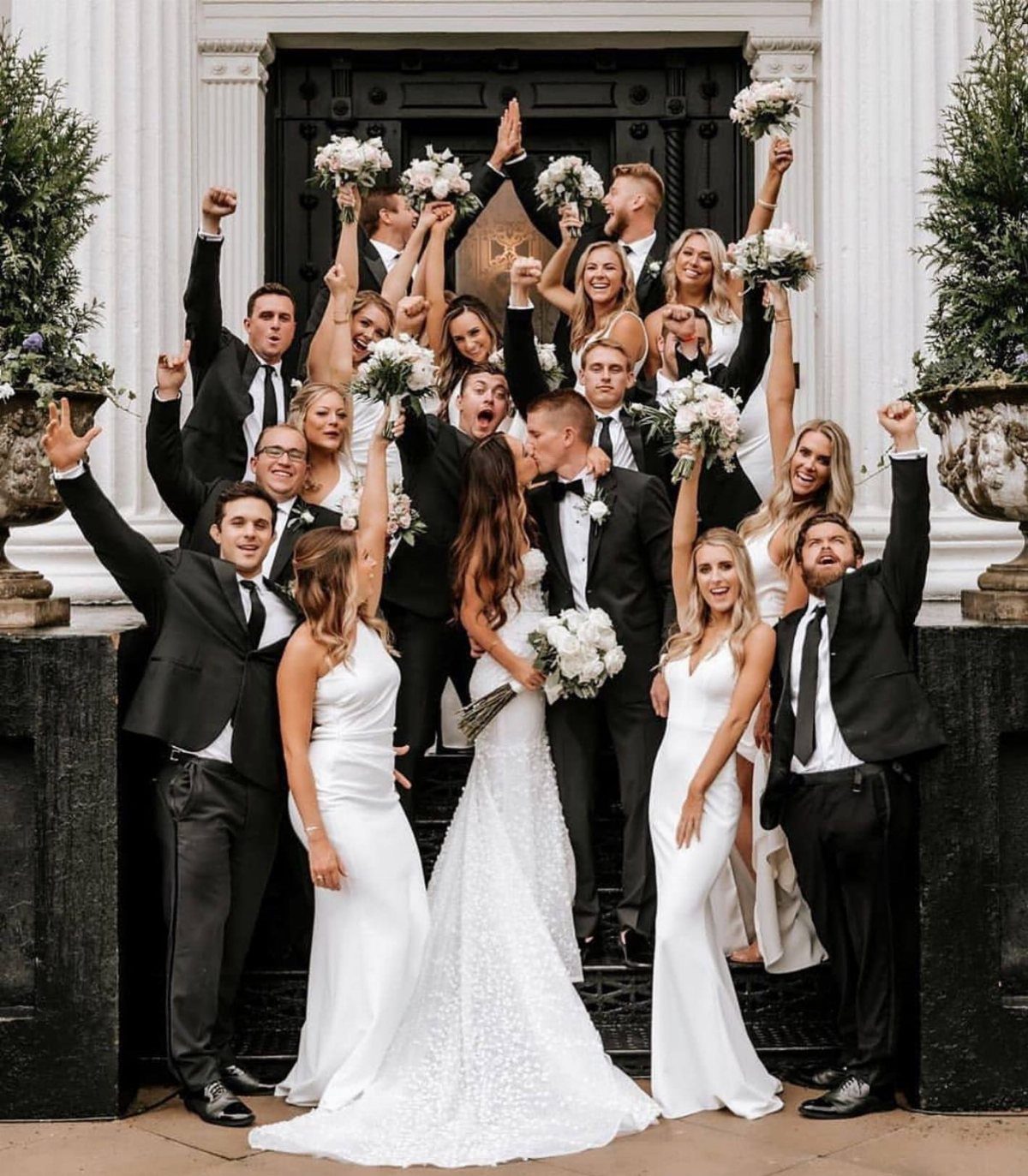 Wedding party in black suits and white dresses posing on black steps.