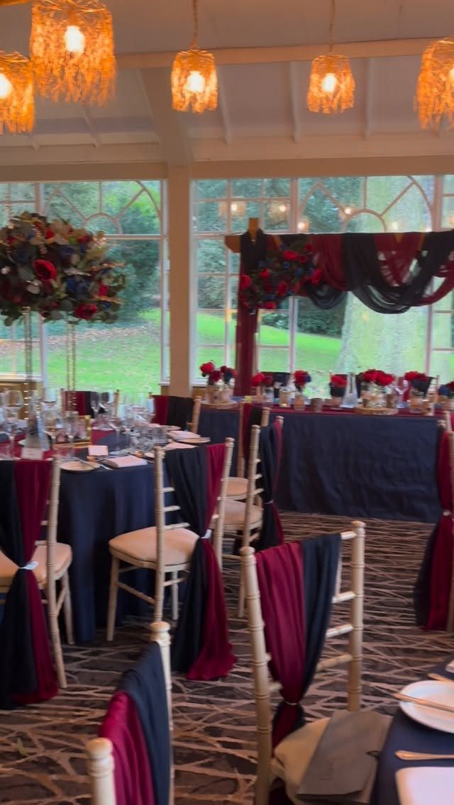 Navy blue and burgundy wedding table settings with red floral centerpieces and sashes.