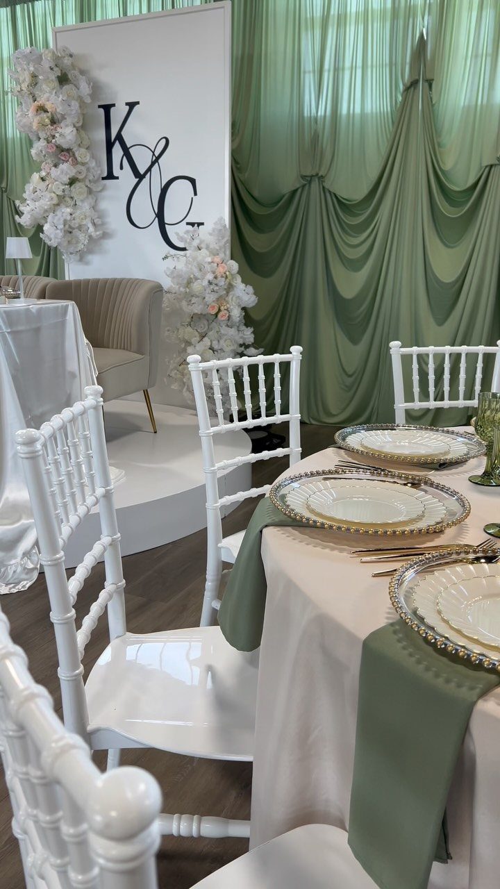 Wedding table setting with sage green runners, white chairs, and gold-rimmed plates.