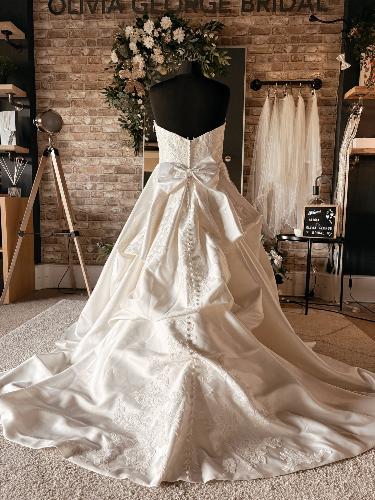 White satin wedding dress with a bustle and bow on a bridal mannequin.