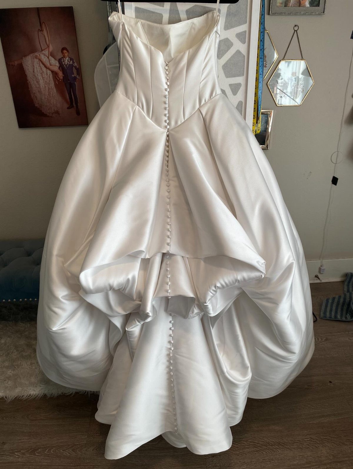 White satin wedding dress hanging from the back showing a centered bustle