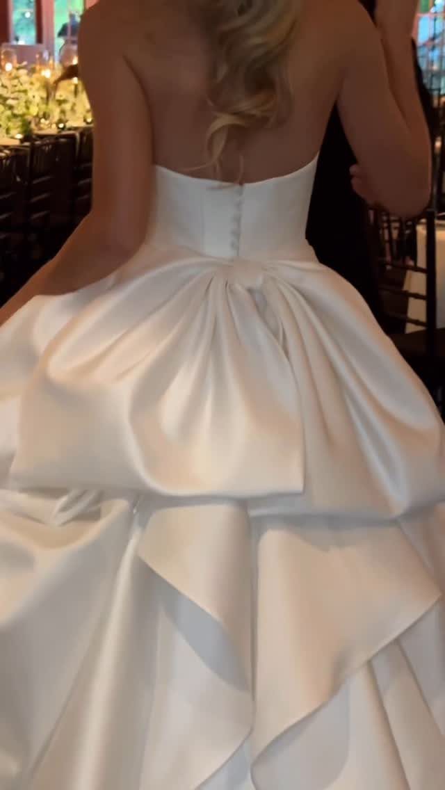 White satin wedding dress with a voluminous gathered bustle on the back skirt.