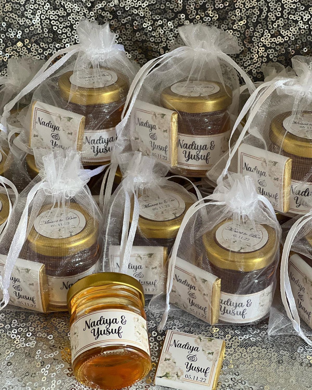 Small honey jars with gold lids and honey dippers in white organza bags.