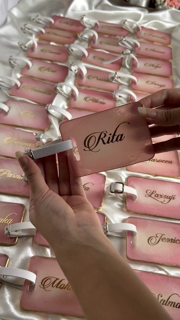 Personalized pink luggage tags with names in cursive on a white satin cloth.