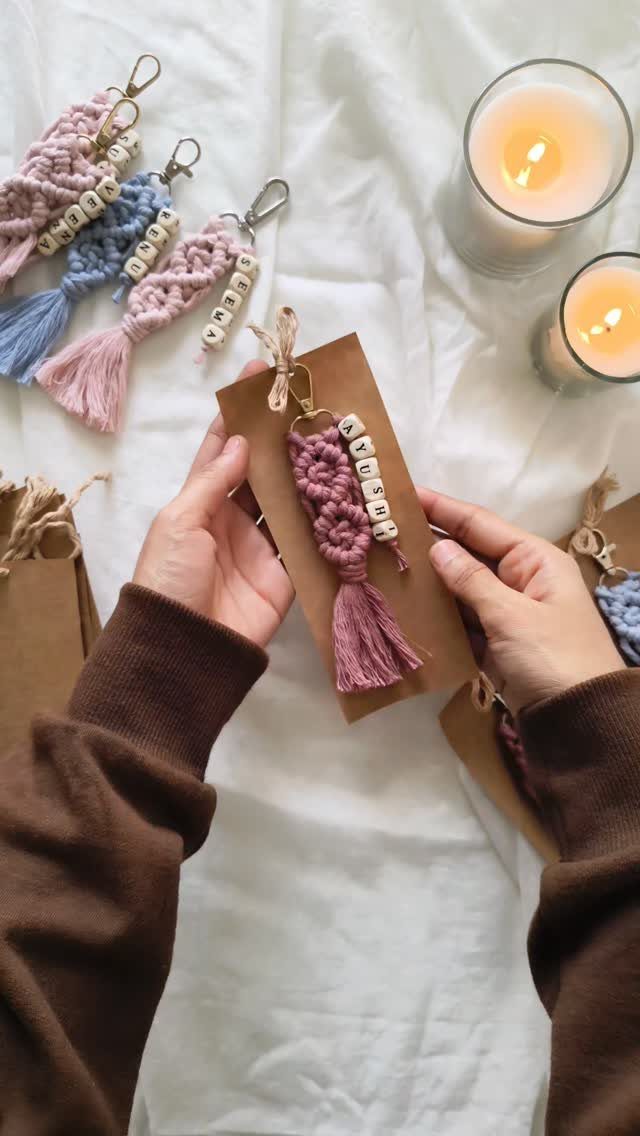 Pink macrame keychain with letter beads held against a brown cardboard backing.