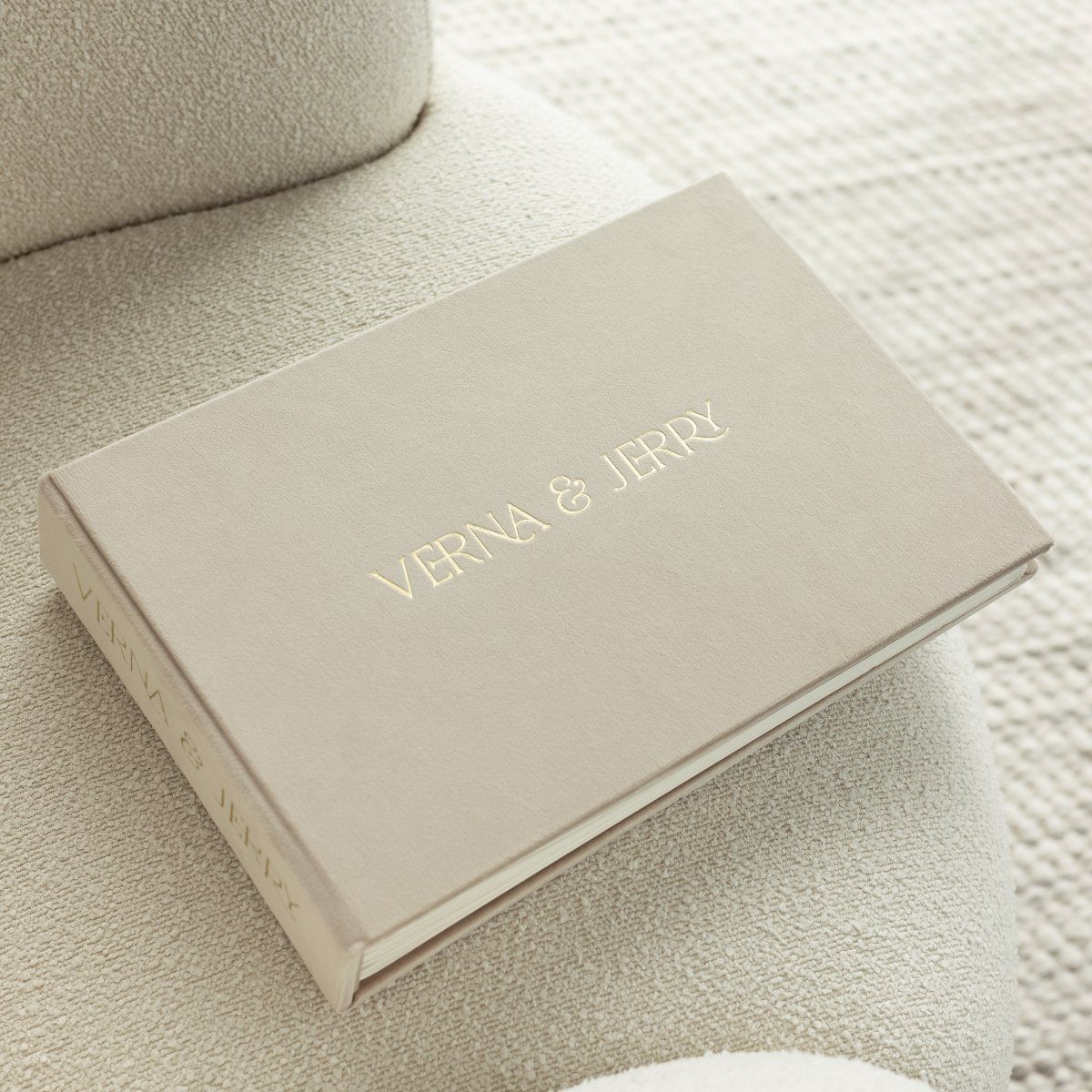 Beige personalized notebook with gold embossed names resting on a textured fabric surface.
