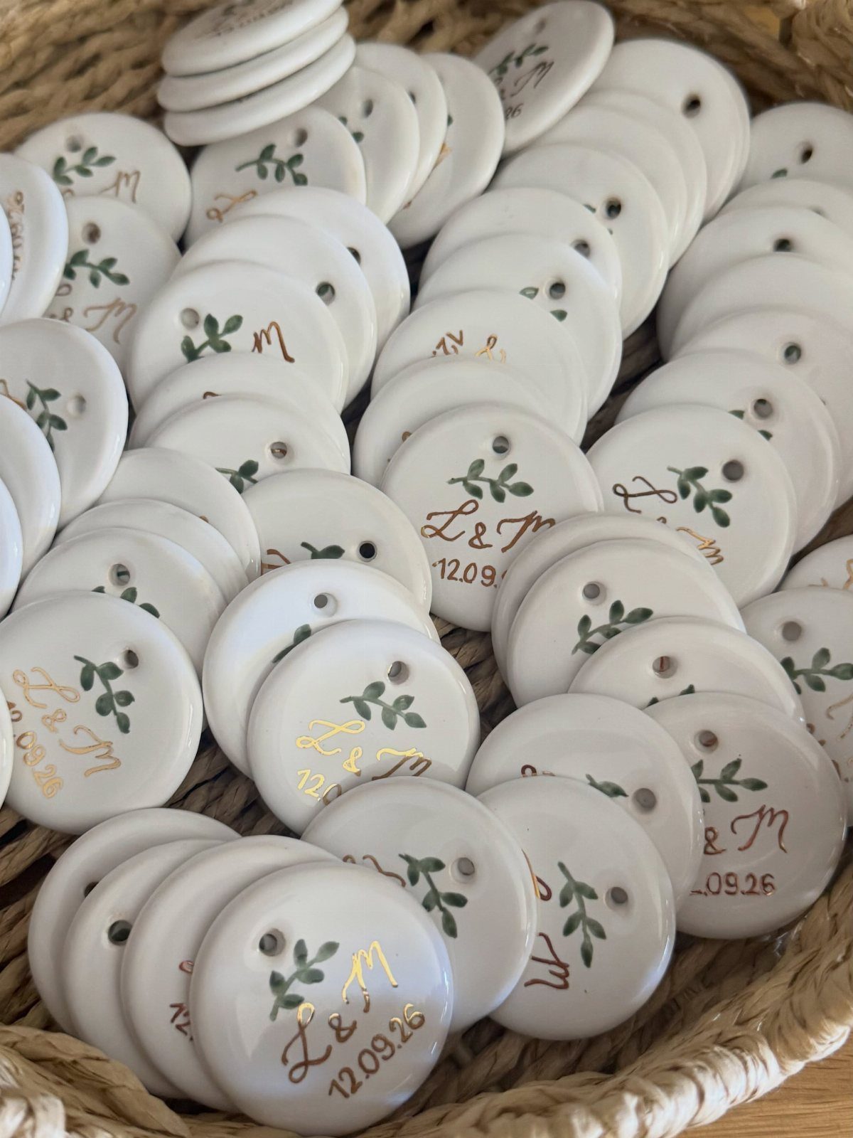 White ceramic round ornaments with gold lettering and green leaves in a wicker basket.