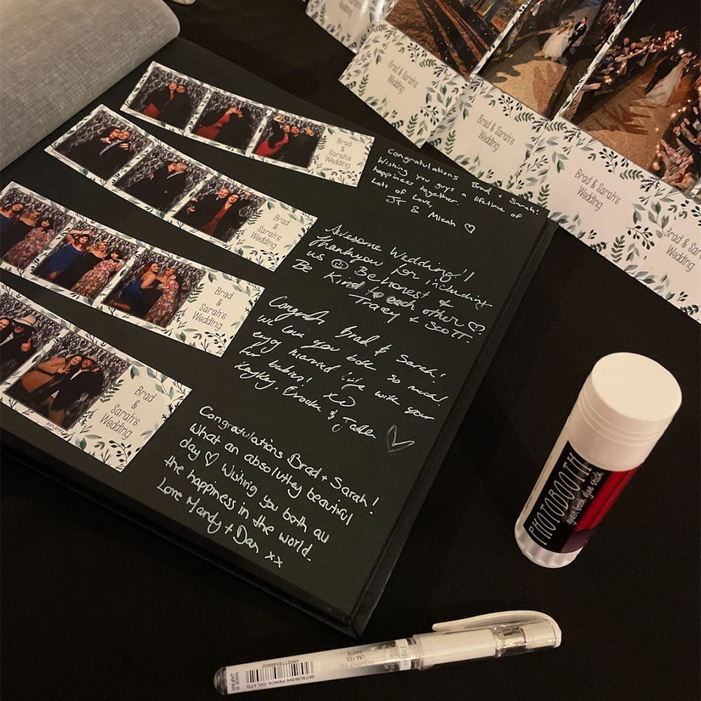 Black wedding guest book with photo booth strips and handwritten white ink messages.