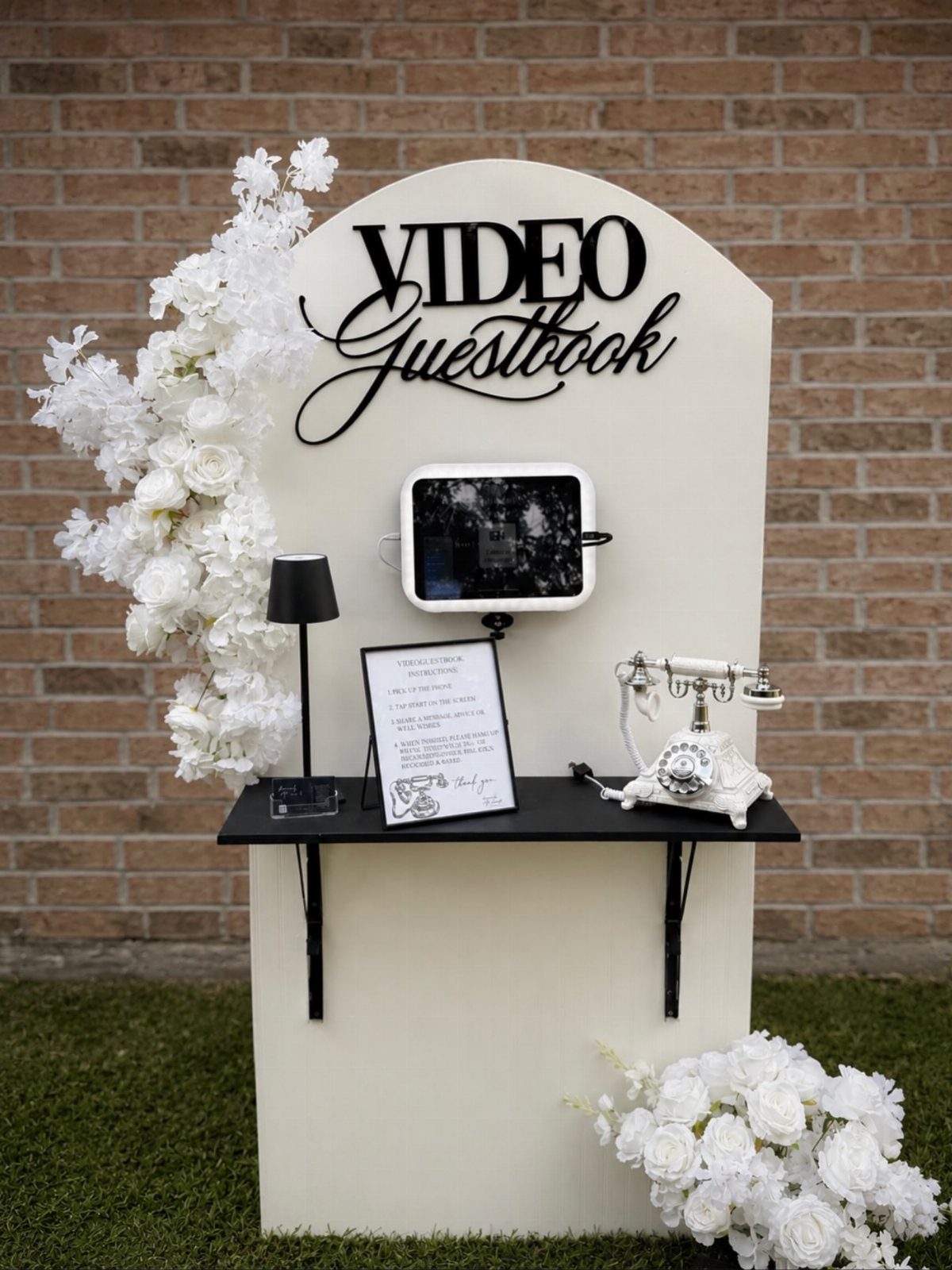 Video guestbook station with a tablet, vintage white phone, and white floral decorations.