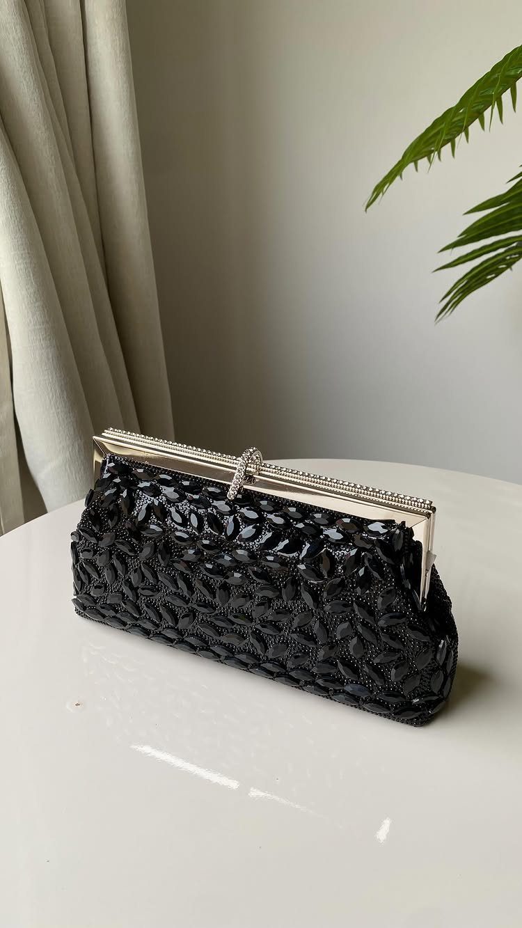 Black beaded rectangular clutch with a silver rhinestone clasp on a white table.