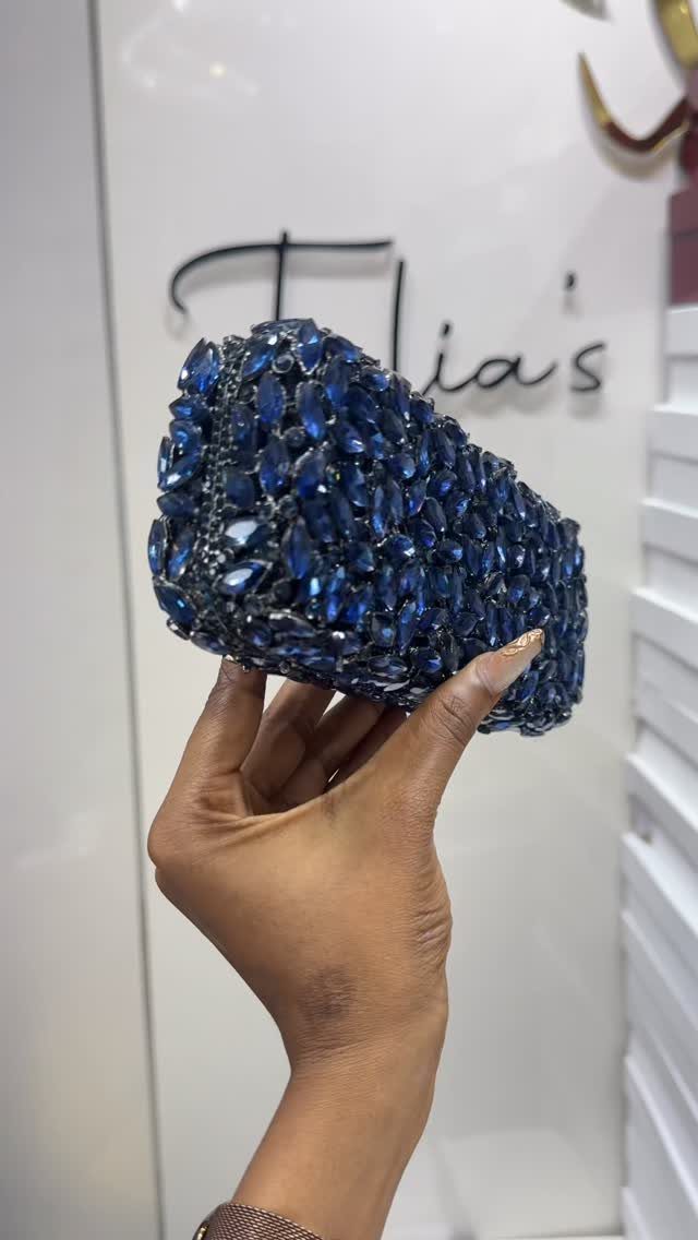 Blue crystal embellished clutch bag held by a hand against a white background