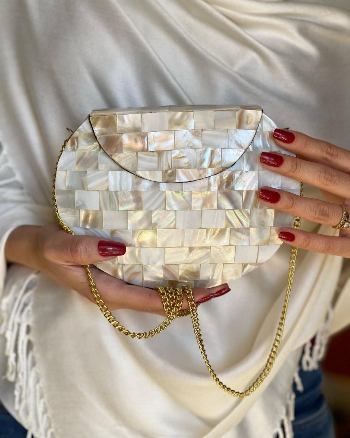 Iridescent mother-of-pearl minaudière clutch with a gold chain held by a person.