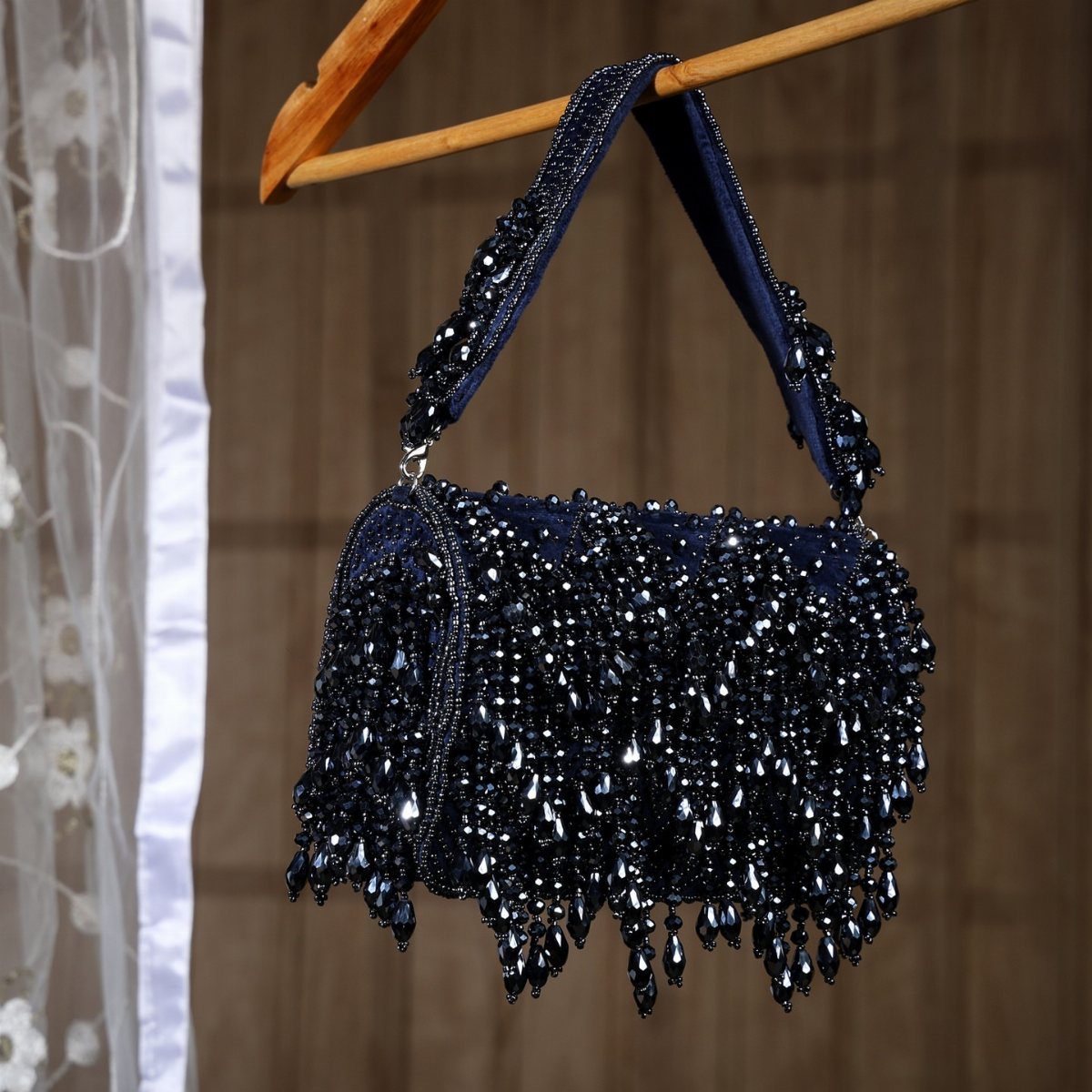 Navy blue beaded handbag with shimmering sequins hanging from a wooden hanger.