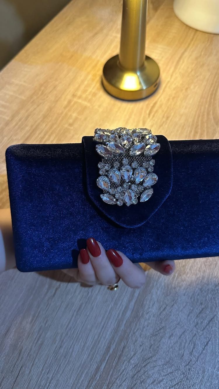 Navy blue velvet clutch bag with a sparkling rhinestone brooch held by a hand.