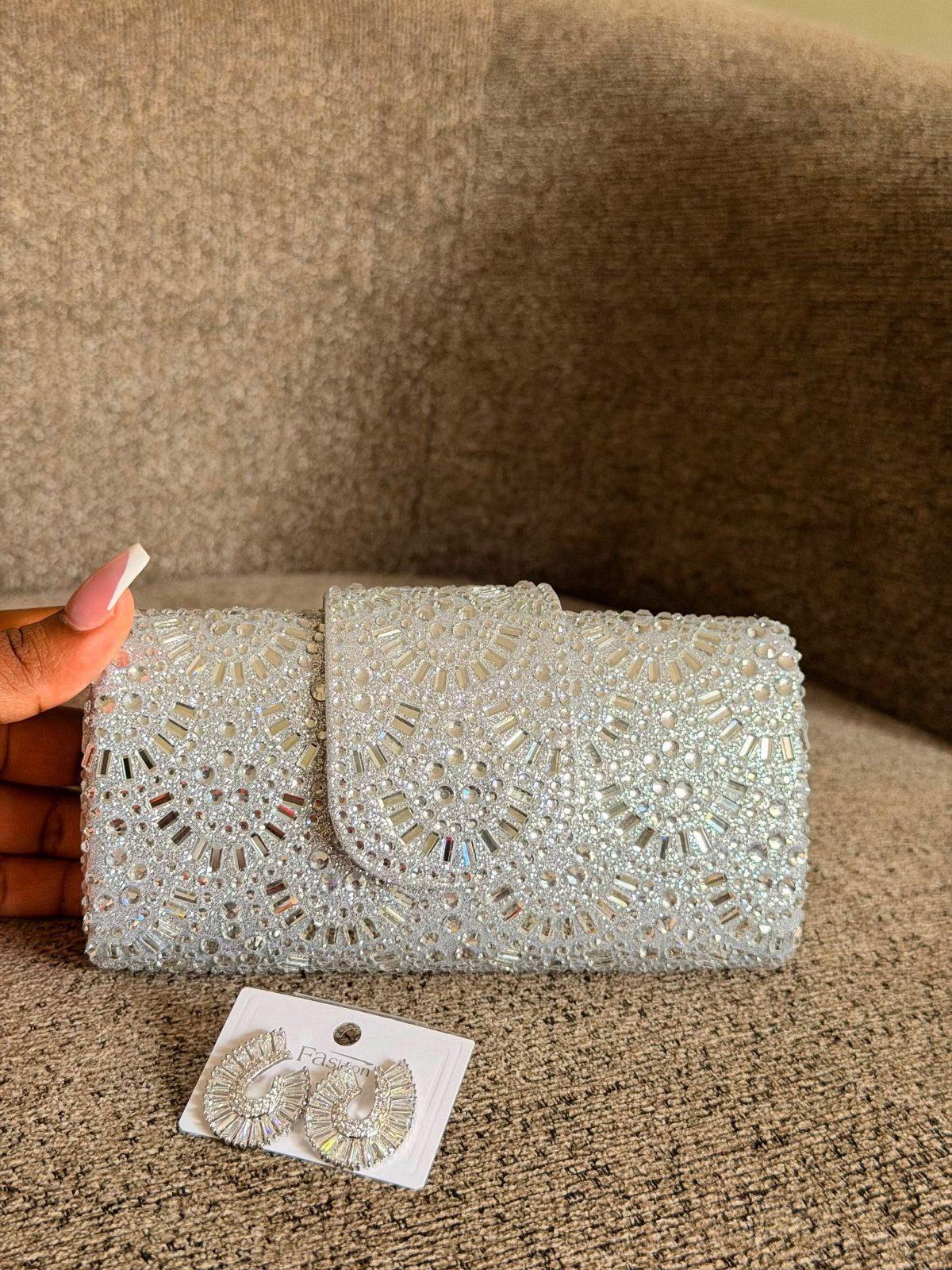 Silver rhinestone clutch bag and matching crystal earrings on a brown textured surface