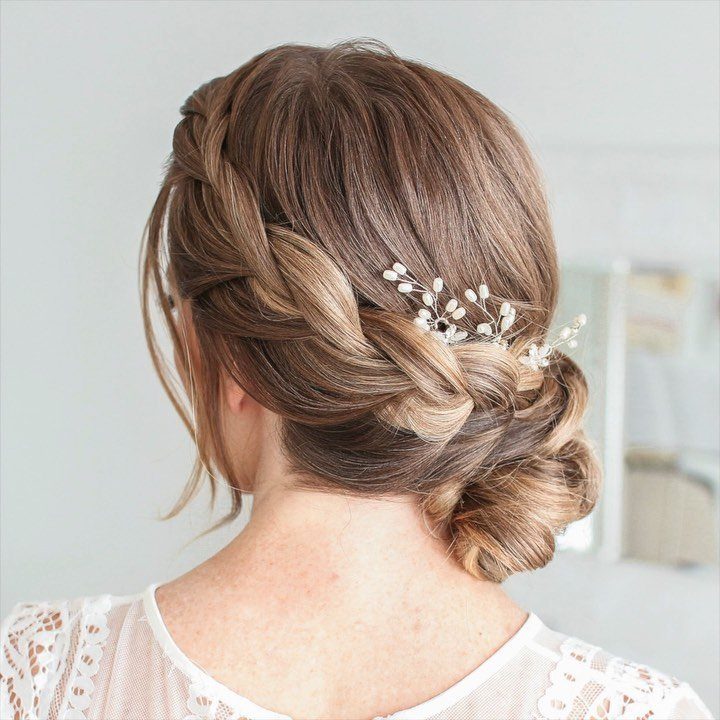 Braided side bun with a white floral hairpiece on light brown hair