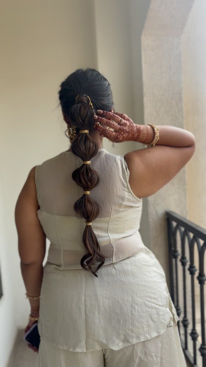Person with a long dark bubble braid accented with gold bands from behind.