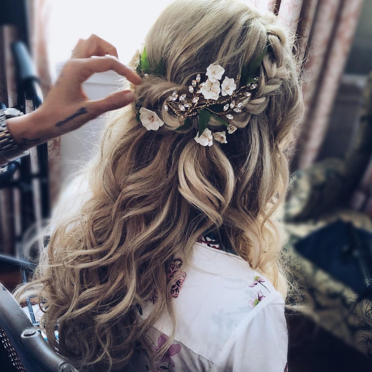 Blonde wavy hair styled in a half-up braided crown with white floral accessories.