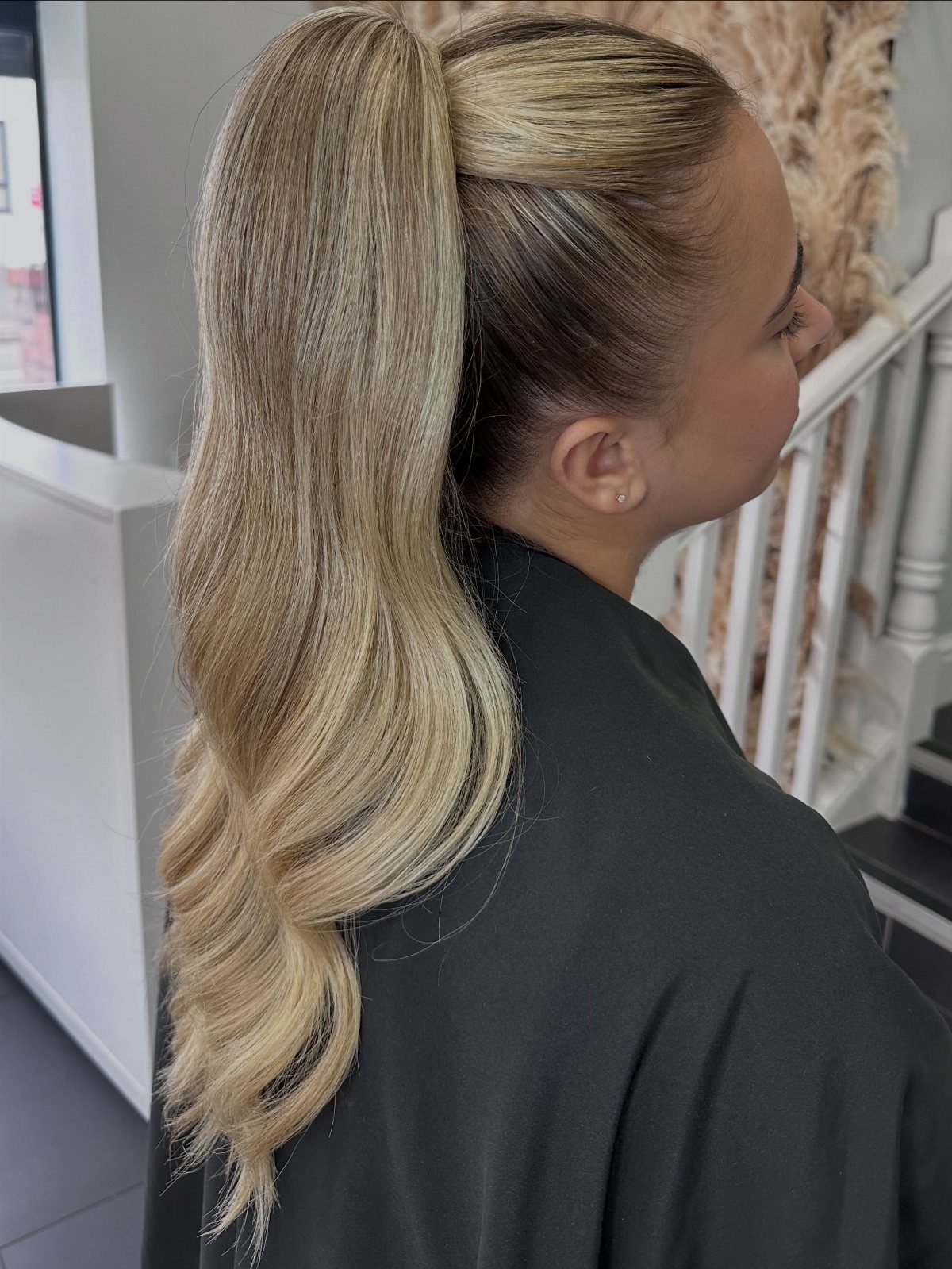 Blonde woman with a high sleek ponytail and wavy ends wearing a black cape.