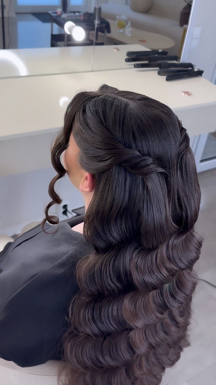 Woman with long dark brown hair styled in glossy, structured Hollywood waves.