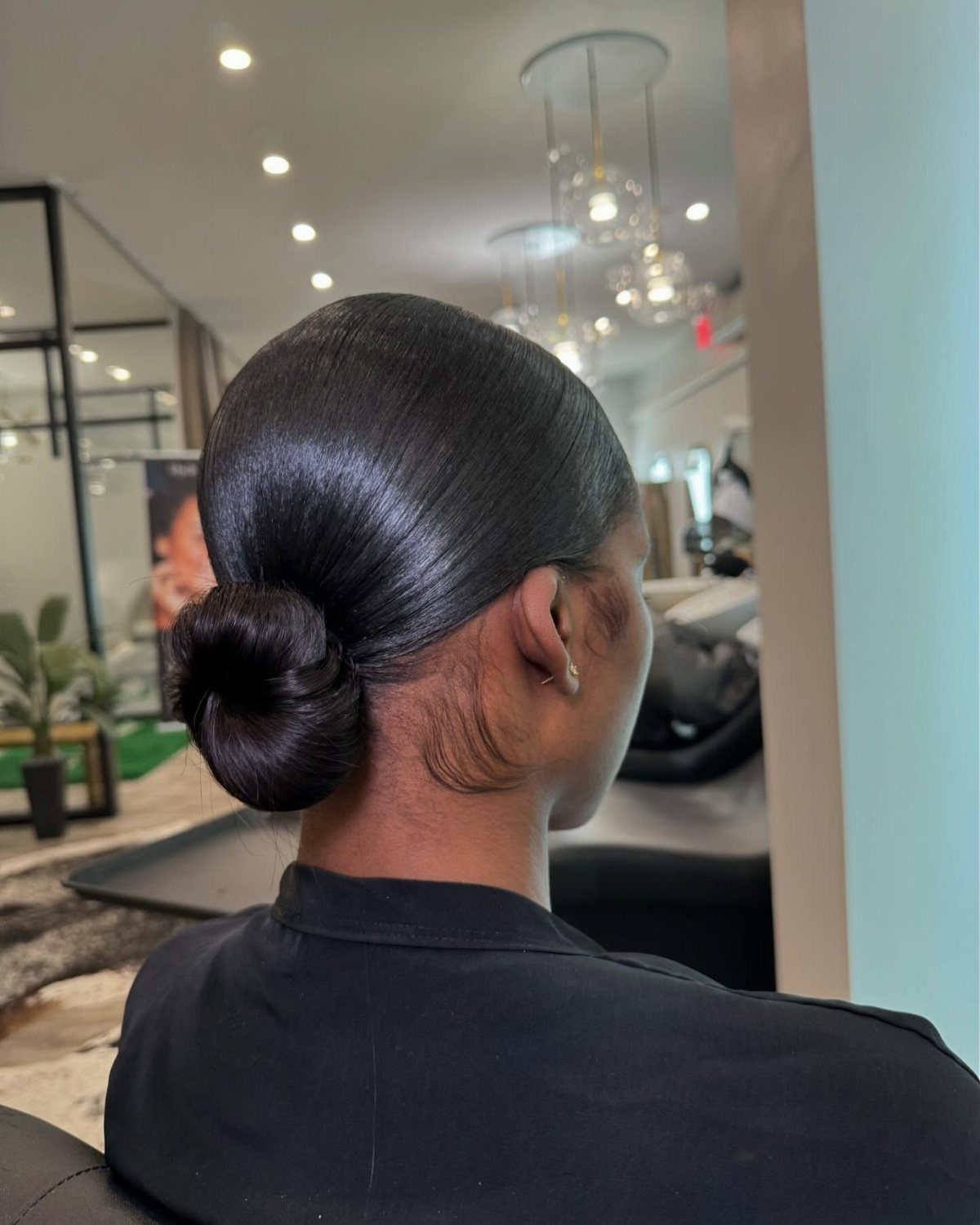 Sleek low bun hairstyle on a person with dark hair in a salon.