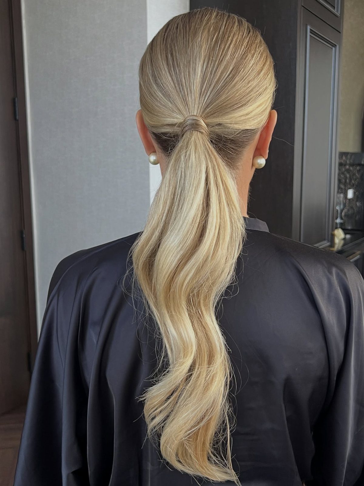Blonde hair styled in a sleek low ponytail with soft waves over black satin.