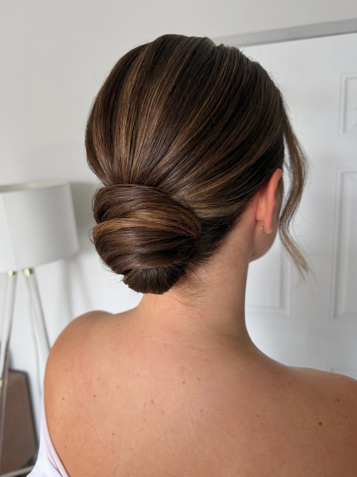 Woman with brown hair styled in a polished low chignon bun from behind.
