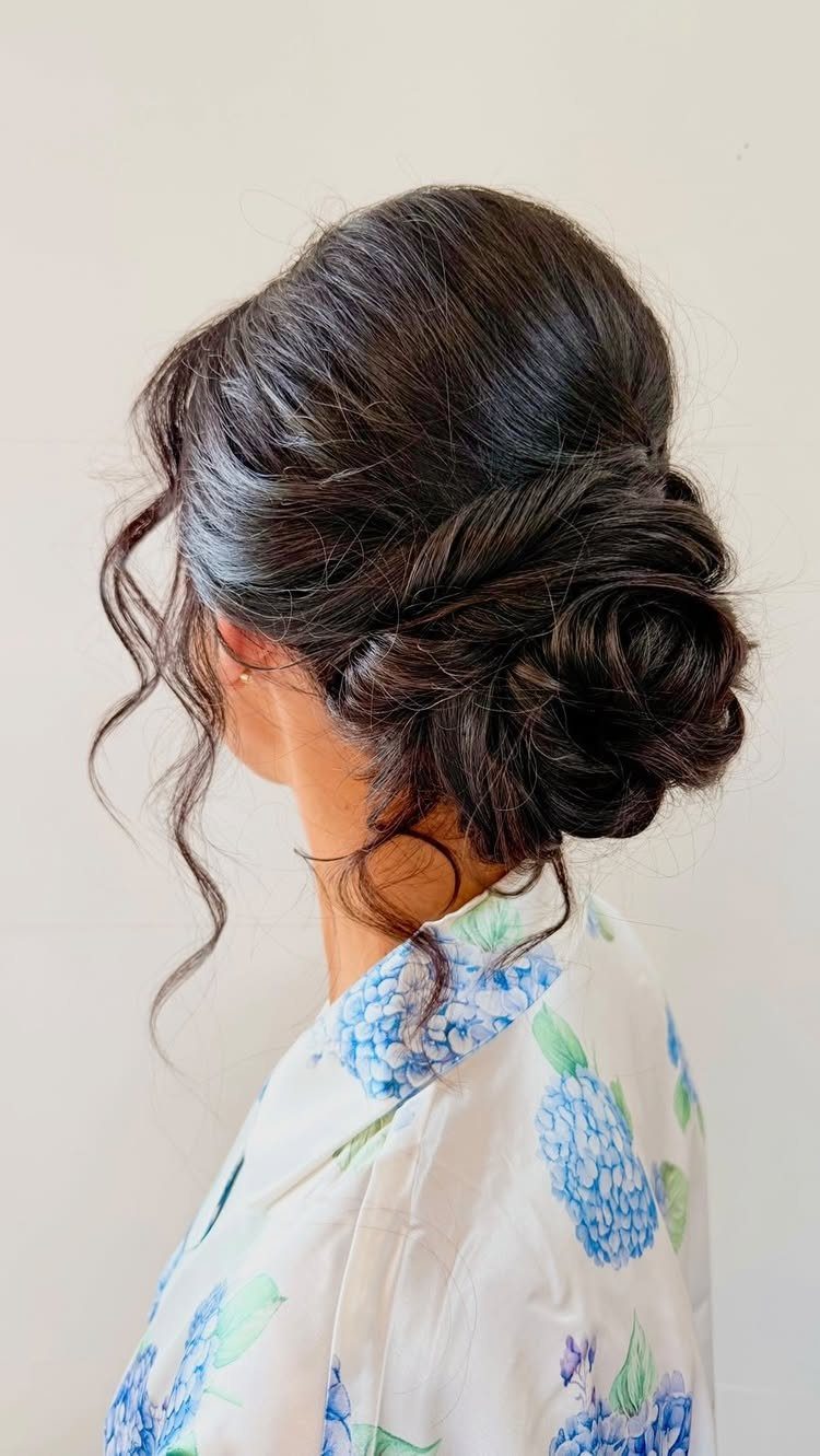 Woman with dark brown hair in a textured low bun and loose curls.