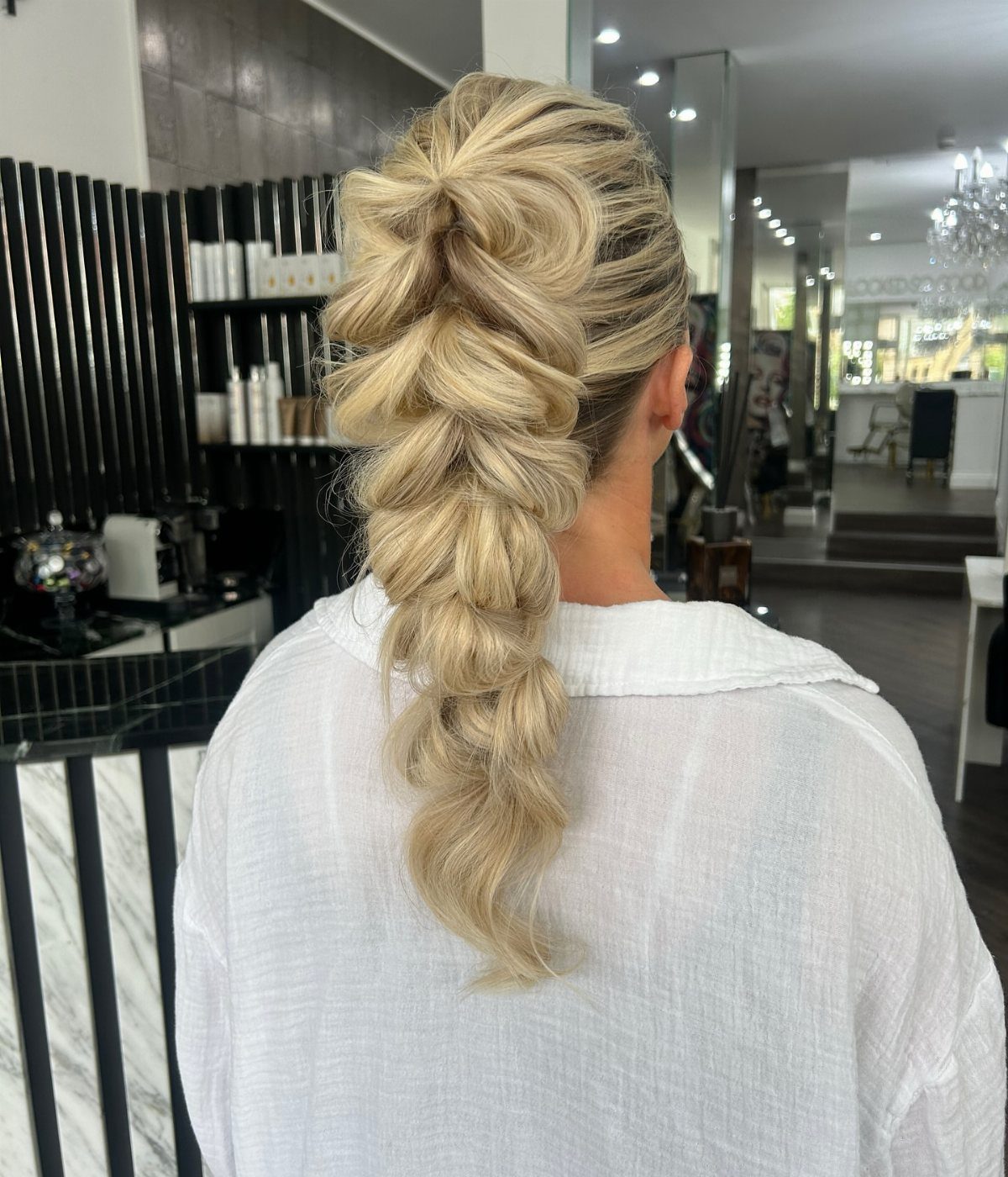 Blonde hair styled in a voluminous braided ponytail with curls in a salon.
