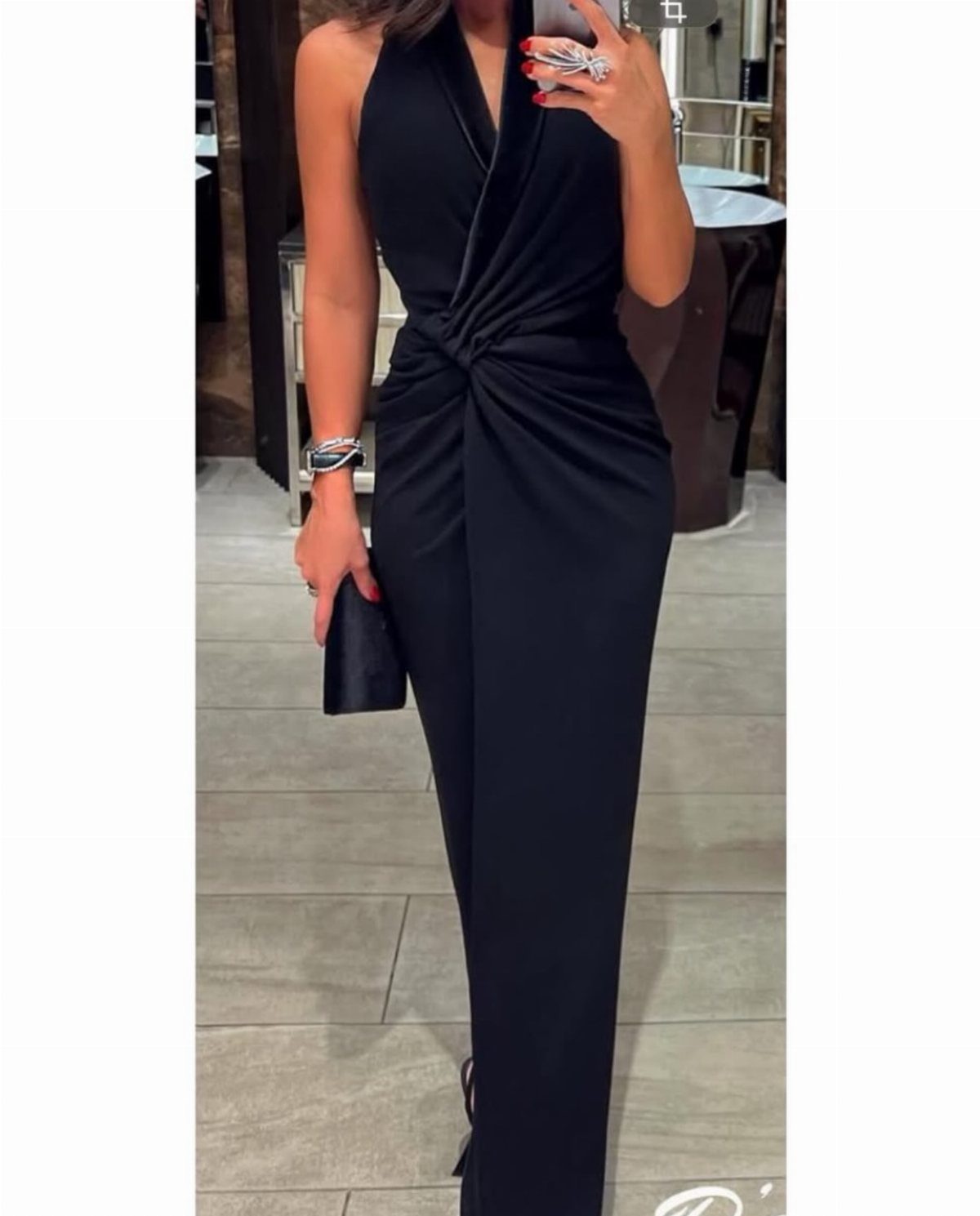Person wearing a black halter-neck jumpsuit with a knotted waist and black clutch.
