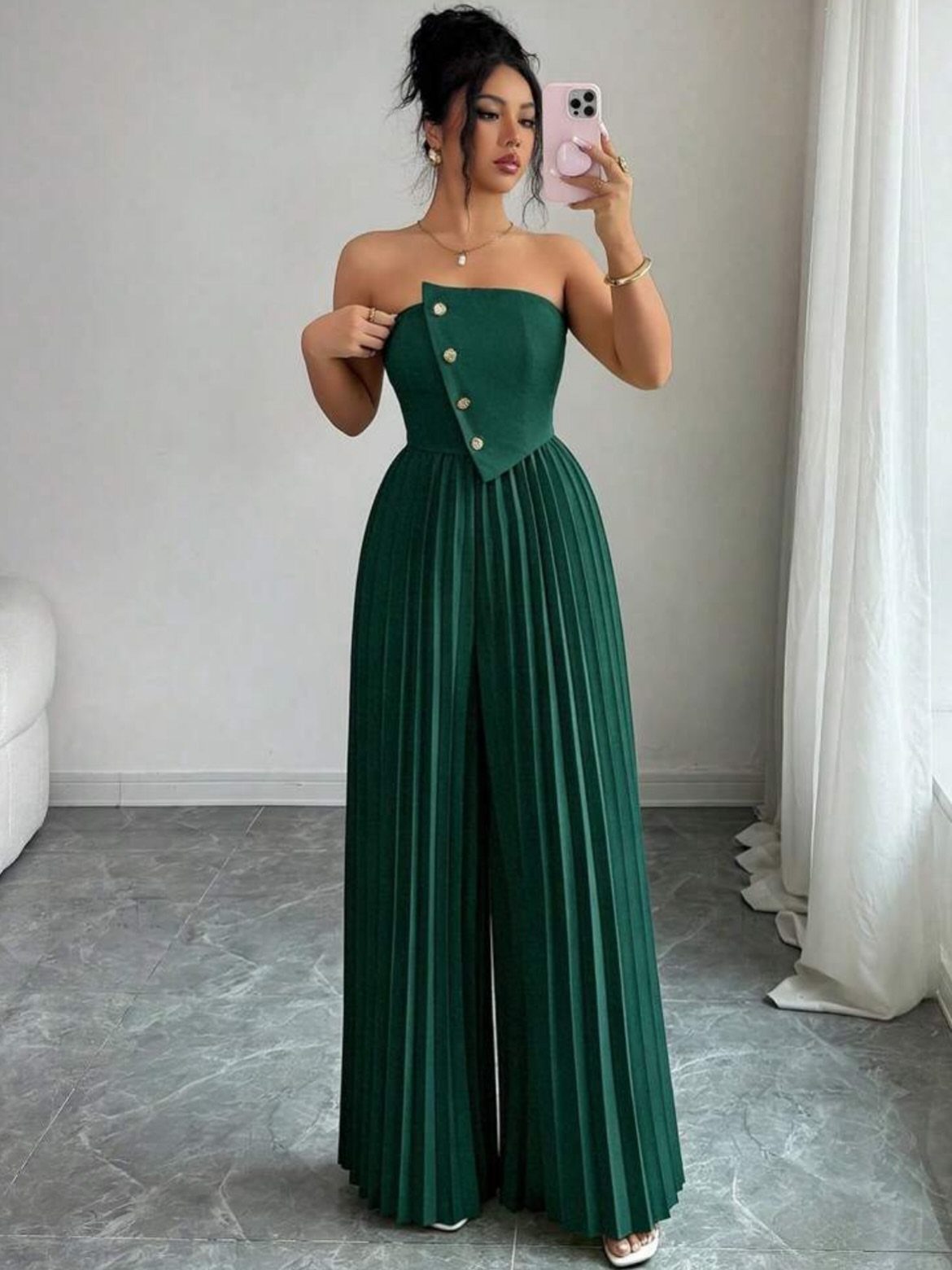 Woman in a strapless dark green pleated wide-leg jumpsuit taking a mirror selfie.