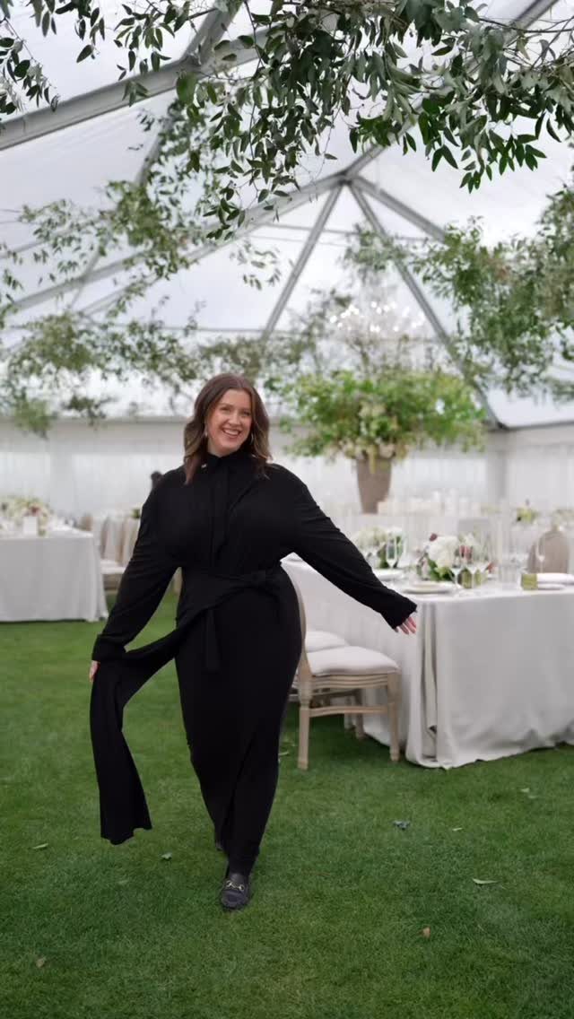 Woman in a long-sleeved black jumpsuit standing inside a white event tent.