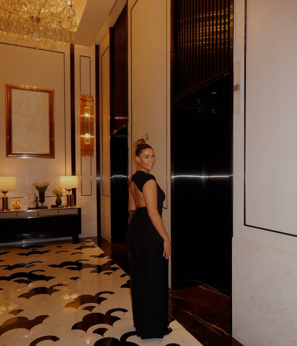 Woman wearing a sleek black wide-leg jumpsuit in a luxury hotel hallway.